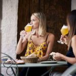 Zwei Frauen sitzen draußen, essen eine Bauernplatte und trinken dazu ein Bier.