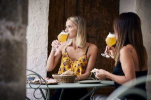 Zwei Frauen sitzen draußen, essen eine Bauernplatte und trinken dazu ein Bier.